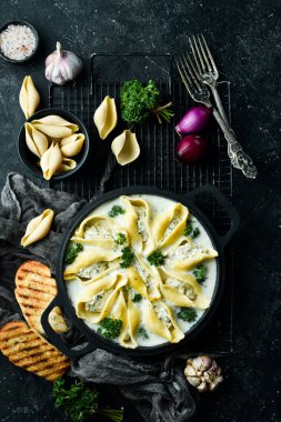 Geleneksel İtalyan yemeği. Et, krema sosu ve parmesanlı kabuk şeklinde makarna. Kızartma tavasında. Taş zeminde. Tarif.