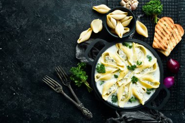 Geleneksel İtalyan yemeği. Et, krema sosu ve parmesanlı kabuk şeklinde makarna. Kızartma tavasında. Taş zeminde. Tarif.