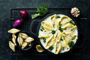 Geleneksel İtalyan yemeği. Et, krema sosu ve parmesanlı kabuk şeklinde makarna. Kızartma tavasında. Taş zeminde. Tarif.