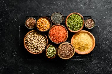 Legumes, farklı fasulye türlerinden oluşan bir set, mercimek ve bezelye, pirinç ve karabuğday siyah arka planda, üst manzara. Sağlıklı ve besleyici gıda kavramı