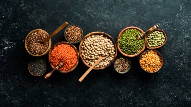 Legumes, farklı fasulye türlerinden oluşan bir set, mercimek ve bezelye, pirinç ve karabuğday siyah arka planda, üst manzara. Sağlıklı ve besleyici gıda kavramı