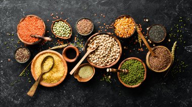 Legumes, farklı fasulye türlerinden oluşan bir set, mercimek ve bezelye, pirinç ve karabuğday siyah arka planda, üst manzara. Sağlıklı ve besleyici gıda kavramı