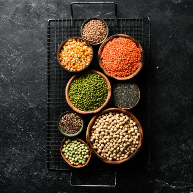 Kâselerdeki organik tahıllar: nohut, fasulye, mercimek. Sağlıklı yiyecekler. Siyah taştan bir arka planda.