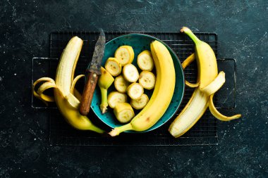Siyah taşlı arka planda bir kasede dilimlenmiş sarı muzlar. Üst görünüm.