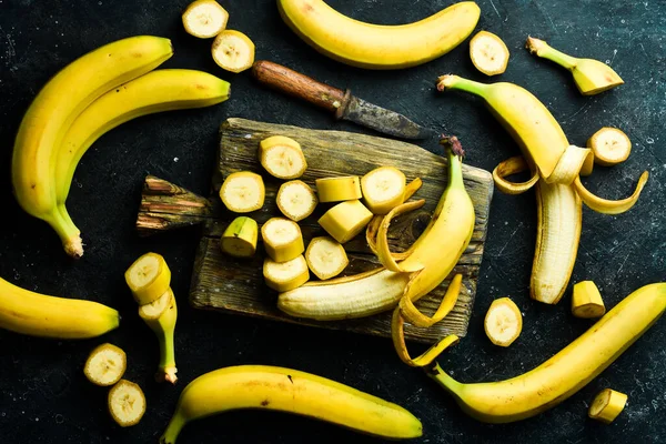 Bunches of yellow bananas sliced in a bowl on a black stone background. Top view.