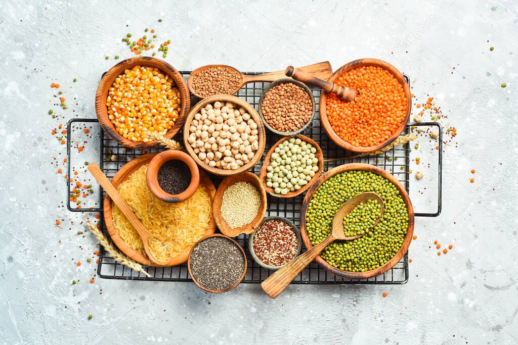 bowls of legumes, lentils, chickpeas, beans, rice and cereals on a stone background, top view.