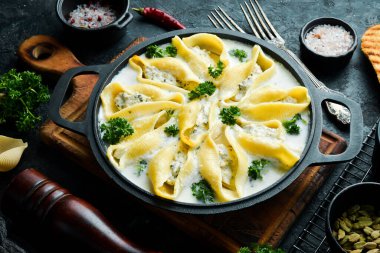 Geleneksel İtalyan yemeği. Et, krema sosu ve parmesanlı kabuk şeklinde makarna. Kızartma tavasında. Taş zeminde. Tarif.
