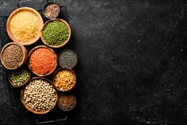 Legumes, farklı fasulye türlerinden oluşan bir set, mercimek ve bezelye, pirinç ve karabuğday siyah arka planda, üst manzara. Sağlıklı ve besleyici gıda kavramı