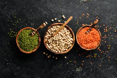 Kâselerdeki organik tahıllar: nohut, fasulye, mercimek. Sağlıklı yiyecekler. Siyah taştan bir arka planda.