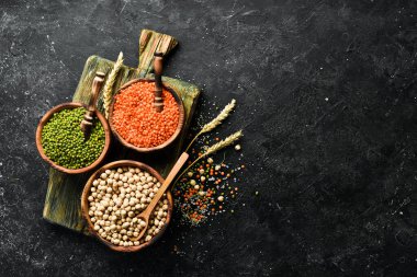Kâselerdeki organik tahıllar: nohut, fasulye, mercimek. Sağlıklı yiyecekler. Siyah taştan bir arka planda.