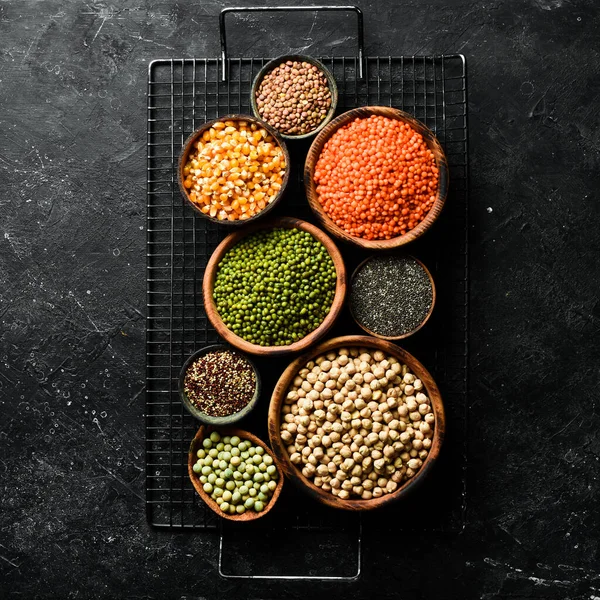 Kâselerdeki organik tahıllar: nohut, fasulye, mercimek. Sağlıklı yiyecekler. Siyah taştan bir arka planda.
