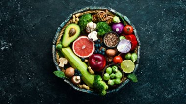 Tahta bir kutuda sağlıklı yiyecek seti: yeşil sebzeler, avokado, brokoli, fındık, mantar, dut ve ıspanak. Siyah taştan bir arka planda. Üst Manzara. Boşluğu kopyala.