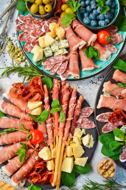 Antipasto aperatif seti: İspanyol jamonu, İtalyan jambonu, peynir seti, zeytin, fesleğen ve atıştırmalık. Üst Manzara. Gri taştan bir arka planda.