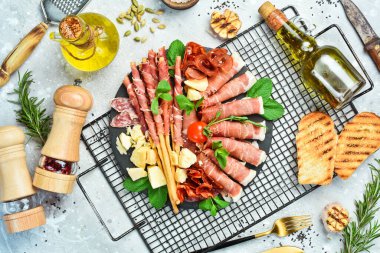 Antipasto tabağı soğuk et, prosciutto, parmesan peyniri ve peynirli Grissini ekmek çubuğu. Taş bir arka planda.