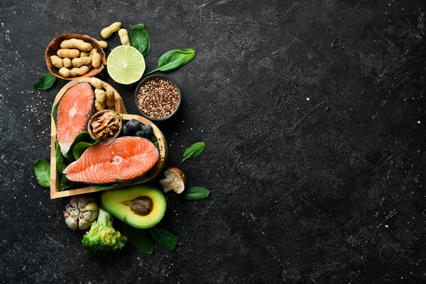 Heart health foods: salmon, avocados, blueberries, broccoli, nuts and mushrooms. On a black stone background. Top view. Copy space.