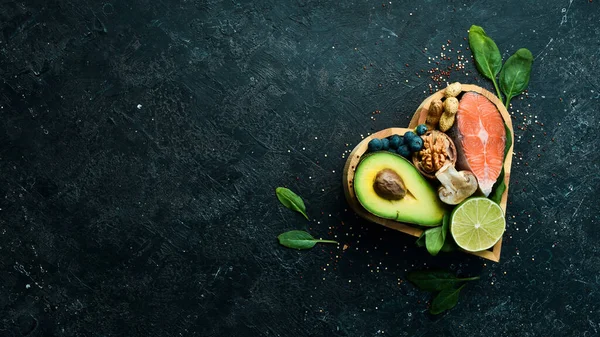 Heart health foods: salmon, avocados, blueberries, broccoli, nuts and mushrooms. On a black stone background. Top view. Copy space.