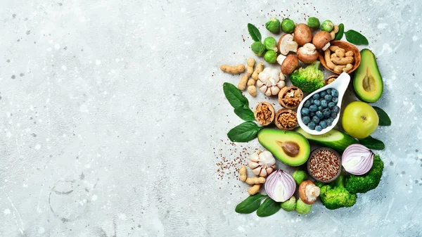 Vegetables and fruits: avocado, green broccoli, nuts, mushrooms, berries and green apples, quinoa. Healthy food. On a gray stone background. Top view.