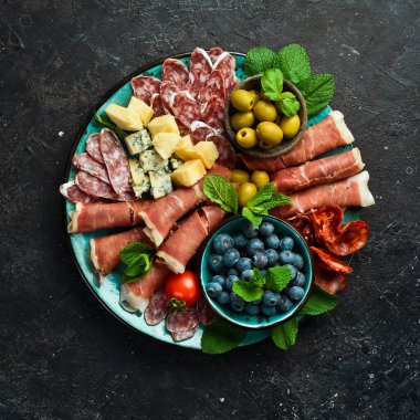 Farklı çeşit peynir ve jambon, prosciutto, jamon salamı ve aperatiflerle dolu bir tabak. Antipasto ya da aperatif parti konsepti. Gri taştan bir arka planda.