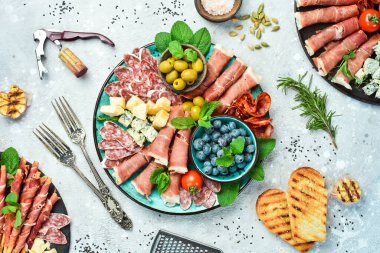 Farklı çeşit peynir ve jambon, prosciutto, jamon salamı ve aperatiflerle dolu bir tabak. Antipasto ya da aperatif parti konsepti. Gri taştan bir arka planda.