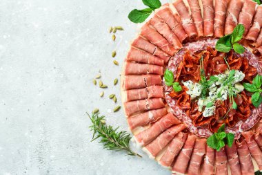 Geleneksel İspanyol mezeleri ya da ahşap tepside İtalyan antipastisi. Jambon ve jambon. Gri taştan bir arka planda.