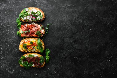 Siyah bir arka planda domatesli, jambonlu, sebzeli ve peynirli renkli sandviçler. Allah 'ım. Üst görünüm.