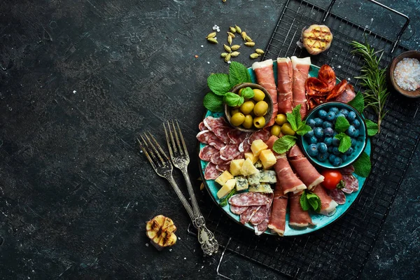 Italian snacks. Plate with cheese and ham, prosciutto, jamon salami, and snacks. On a black stone background.