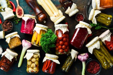 Terbiye edilmiş sebze. Uzun vadeli depolama için cam kavanozlardaki çeşitli sebzeleri tuzlamak. Masanın üzerinde mayalanmış yeşil sebzeler var. Taş zeminde. Üst görünüm.