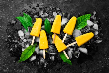 Buzlu dondurulmuş sarı buzlu dondurma. Soğuk yaz meyveli tatlılar. Siyah taştan bir arka planda. Üst görünüm.