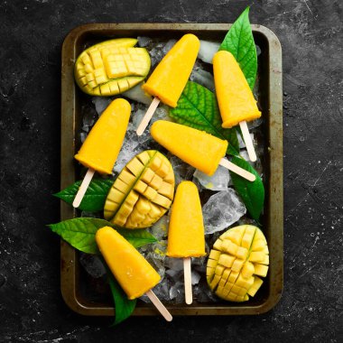 Tepside donmuş mango dondurması. Soğuk yaz tatlıları. Siyah taştan bir arka planda. Üst görünüm.