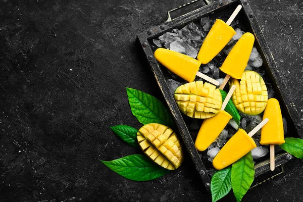 Frozen mango popsicles on a tray. Cold summer sweets. On a black stone background. Top view.