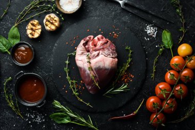 Çiğ domuz kalbi baharat ve bitkilerle pişirmeye hazır. - Et. Siyah bir arkaplanda.