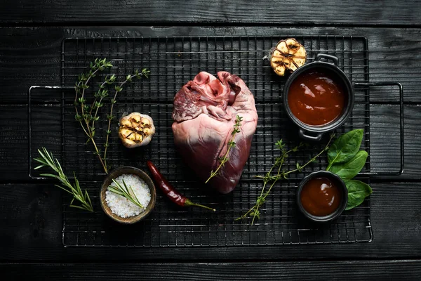 Raw pork heart is ready to cook with spices and herbs. Meat. On a black background.