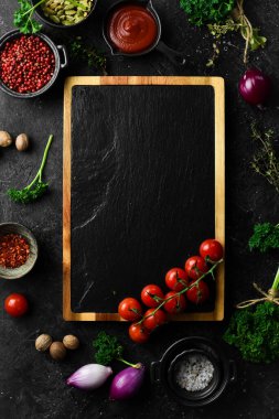 Taştan siyah aşçılık geçmişi. Sebze ve baharatlı mutfak tahtası. Siyah taştan bir arka planda. Üst görünüm.