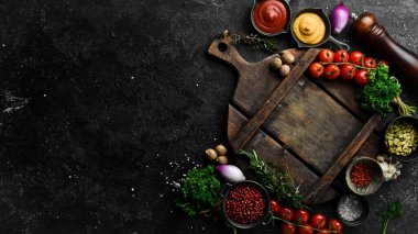 Taştan siyah aşçılık geçmişi. Sebze ve baharatlı mutfak tahtası. Siyah taştan bir arka planda. Üst görünüm.