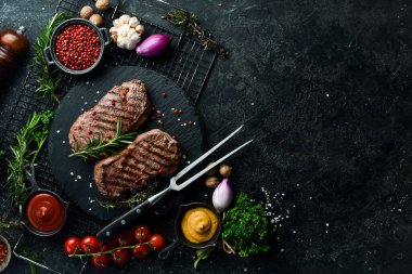 Izgara biftek, otlar ve baharatlar karanlık bir masada. Üst görünüm.