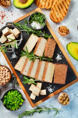 Taze tofu peyniri. Baharatlı füme tofu peyniri. Tahtada parçalara ayrılmış. Vejetaryen sağlıklı yemek. Taş bir arka planda.