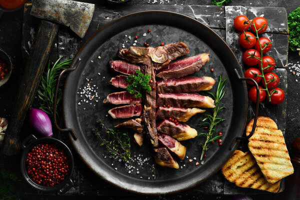 Chopped juicy porterhouse steak or T Bone Steak dry aged of beef Ready to Cook on wooden Board with herbs, pepper and salt. On a black stone background.