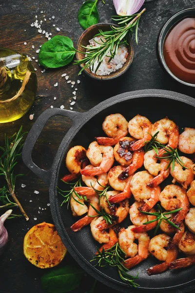 Fried shrimp with garlic and lemon in a pan. Seafood. On a black stone background.