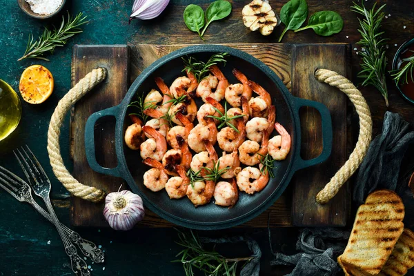 Fried shrimp with garlic and lemon in a pan. Seafood. On a black stone background.