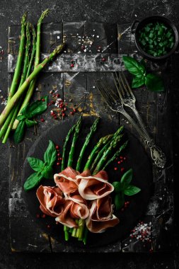 Prosciutto ve fesleğenle ızgara kuşkonmaz. Siyah taştan bir arka planda. Üst görünüm.