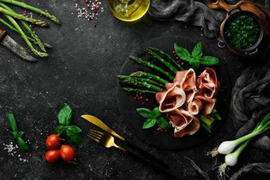 Prosciutto ve fesleğenle ızgara kuşkonmaz. Siyah taştan bir arka planda. Üst görünüm.