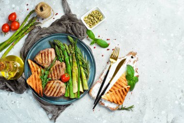 Biftek. Kuşkonmaz, domates ve tostlu dana madalyonu. Siyah taştan bir tabakta.