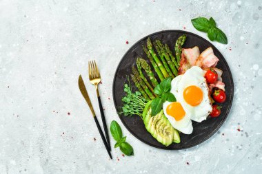 Kahvaltıda. Çırpılmış yumurta, kuşkonmaz, pastırma ve avokado. Siyah taştan bir tabakta.