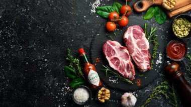 UKRAINE, LVIV - 10 Şubat 2022: Çiğ domuz bifteğiyle birlikte bir şişe acı sos. Üst Manzara. Siyah taştan bir tabakta.