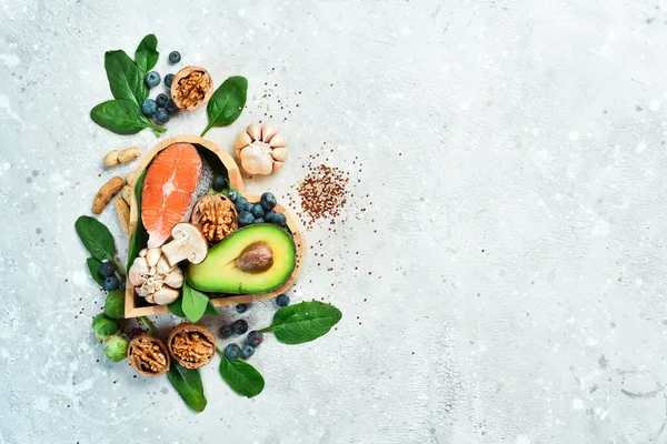 Foods good for the heart: nuts, salmon, avocados, spinach, mushrooms, berries. In a heart-shaped box. On a stone background. Top view. Copy space.