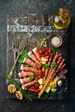 İtalyan malzemeleri: jambon, jambon, salam, parmesan, zeytin, ekmek çubukları. Siyah taştan bir arka planda.