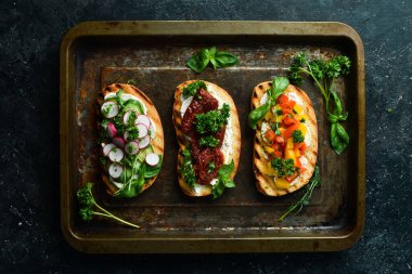 Ev yapımı sandviçler. Siyah bir arka planda domatesli, jambonlu, sebzeli, peynirli sandviç. Üst görünüm.