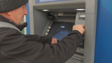 Yetişkin bir adam ATM 'ye kredi kartı sokuyor.
