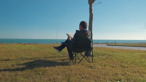 Άνθρωπος ανάγνωση βιβλίο κάθεται στην καρέκλα — Αρχείο Βίντεο