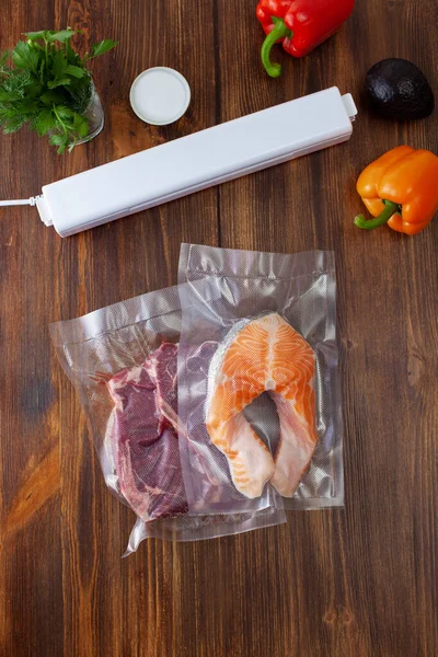 Vacuum cleaner with vacuum bags with a piece of beef and salmon with fresh vegetables on a dark wooden table. Copy space text